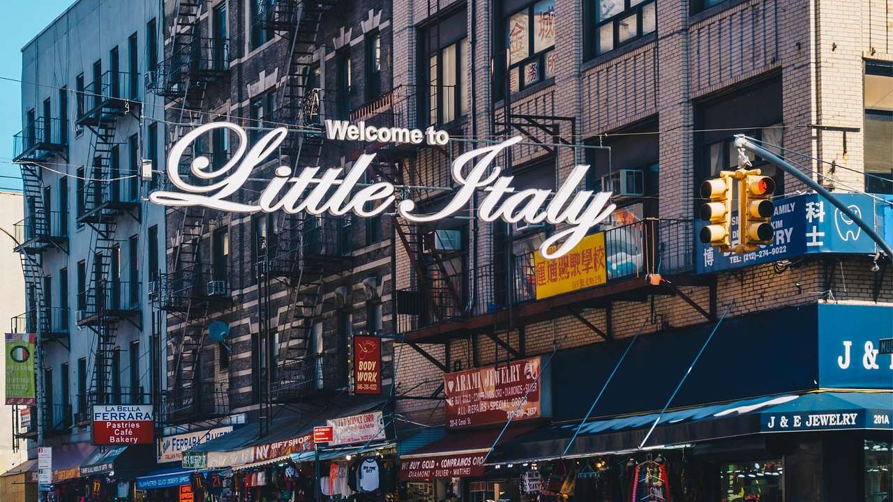 A sign that says "Welcome to Little Italy" above a street with shops and restaurants