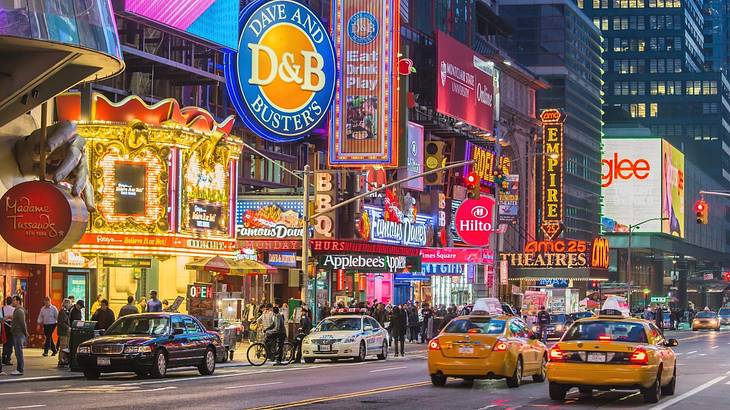 A street with buildings covered in neon signs and yellow taxi cabs in front at night