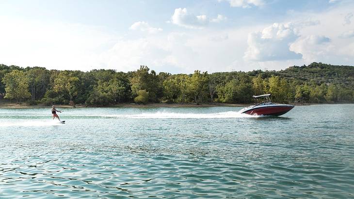 A lake with a boat and someone jet skiing and greenery-covered hills on the shore