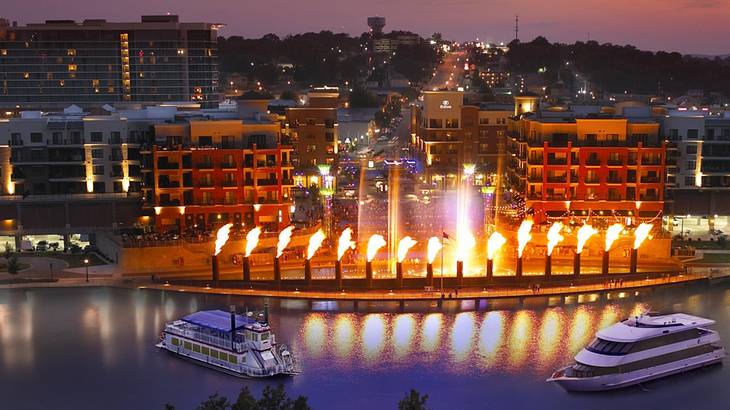 A fire and water display with buildings behind it and water with boats on it in front