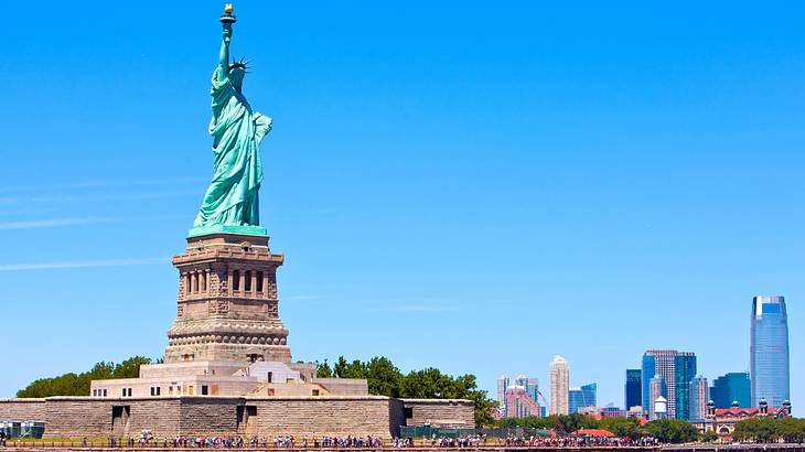 A light-blue statue of a woman holding a torch against a skyline A light-blue statue of a woman holding a torch against a skyline