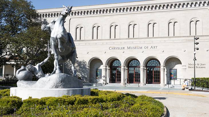 A white sculpture of a horse against a museum building with three arched doors