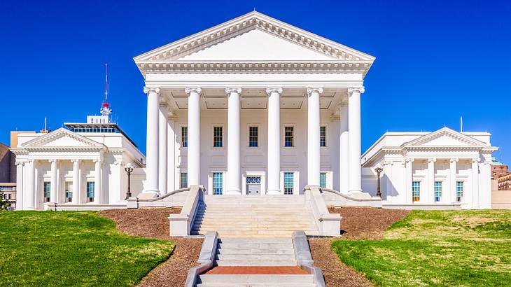 A staircase to a white neoclassical capitol building surrounded by green grass