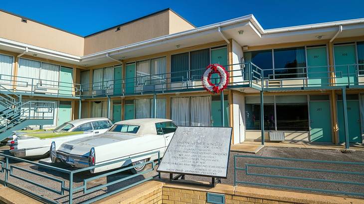 An old-fashioned motel with 1960s-style cars and a historical plaque in front of it
