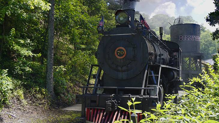 A black train billowing smoke as it slowly moves along tracks