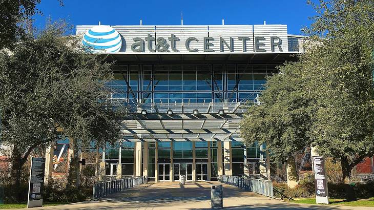 A sports arena that says AT&T Center with a path and trees in front of it