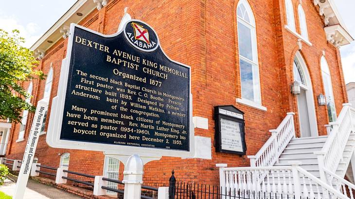 The walls of a red brick building and white steps with a historical plaque in front