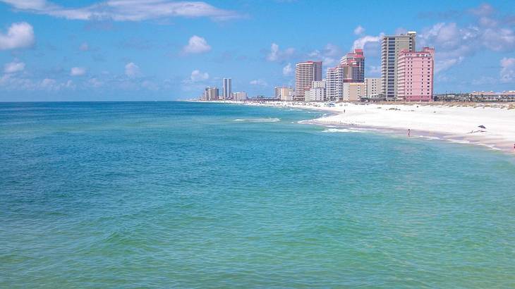 Ocean water next to a white sand beach with some high-rise buildings in the distance