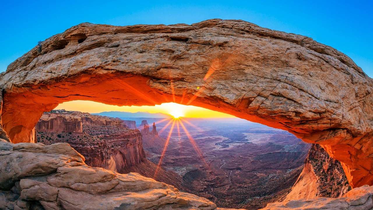 A view of a canyon valley and the sunset through a rock arch