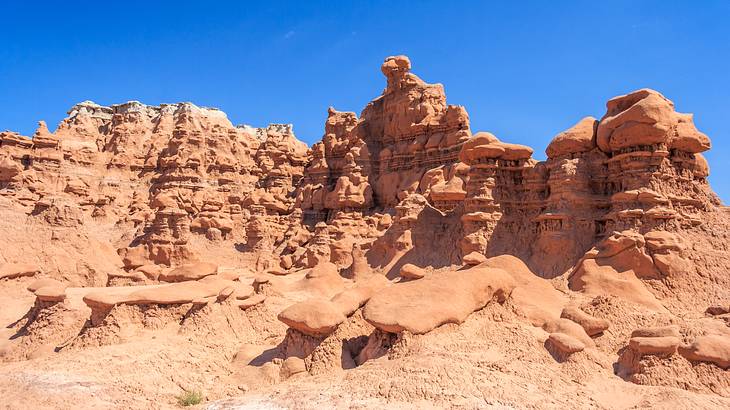 A red sandstone cliff with jagged rock formations under a clear blue sky