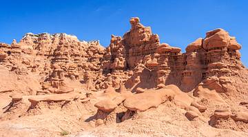 A red sandstone cliff with jagged rock formations under a clear blue sky
