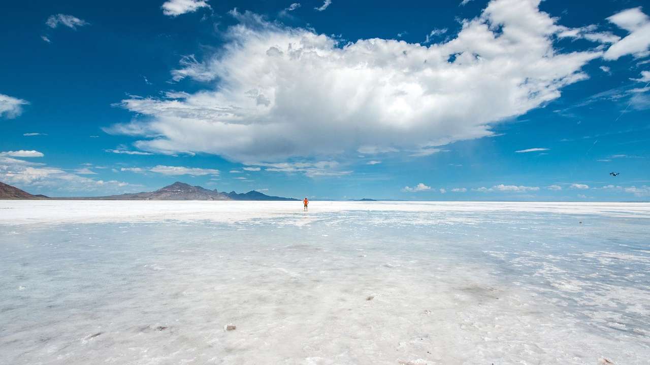 A white salt flat with hills in the distance under a blue sky with a large cloud