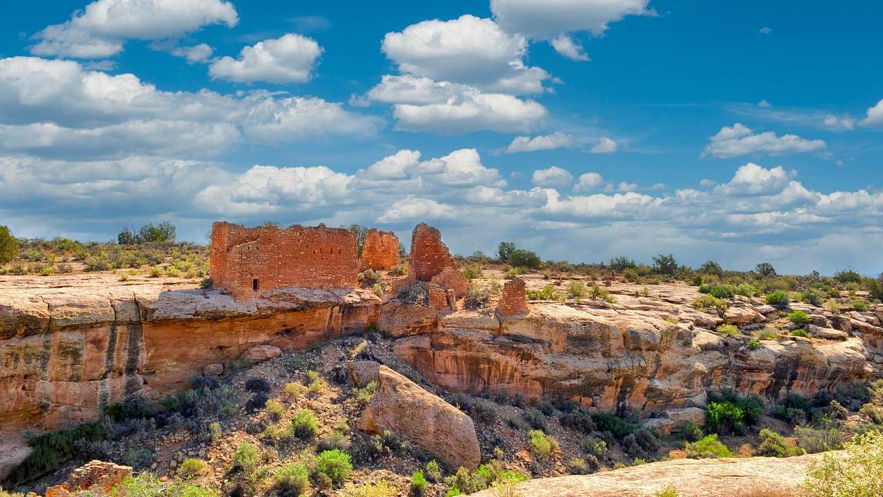 Red sandstone rocks and ruins surrounded by greenery under a blue sky with clouds