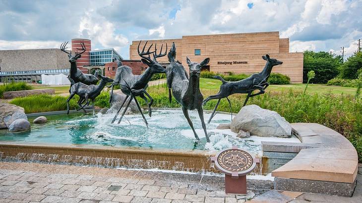 A statue of five deer over a fountain with a museum building behind it