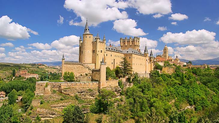 A fortified medieval castle atop a hill, surrounded by greenery, on a nice day