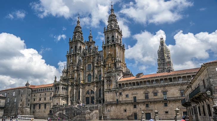 The facade of a cathedral in Gothic and Baroque style against a partly cloudy sky