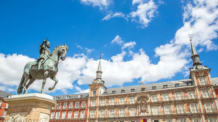 A bronze statue of an equestrian on a pedestal in front of a building on a nice day