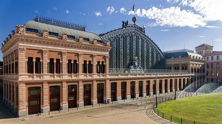 A massive station made of brick, steel, and glass with a grassy field in front