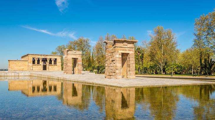 Stone monuments reflected over an artificial pool surrounded by greenery