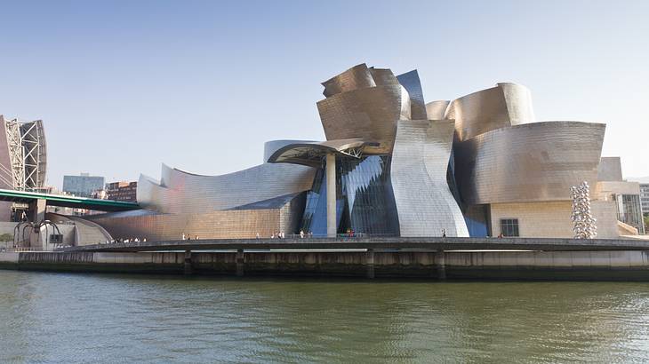 A modern structure made of glass, limestone, and titanium by a river on a clear day