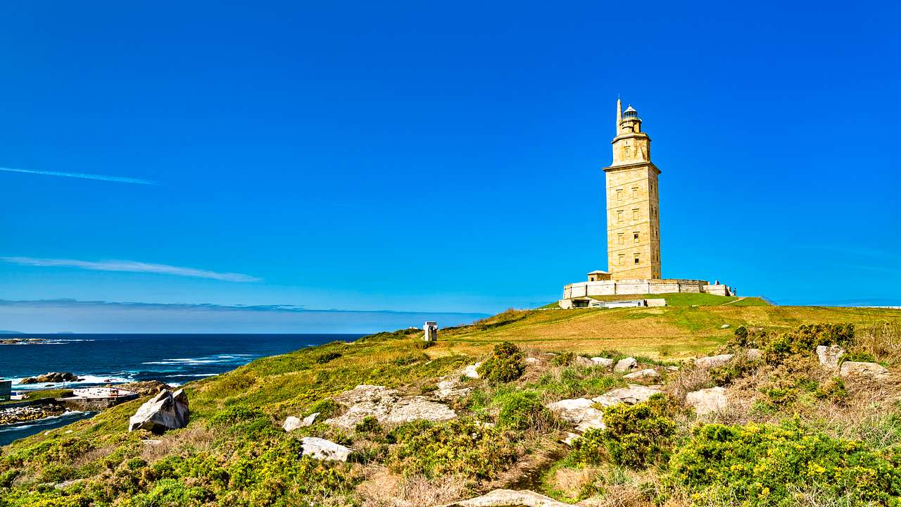 An ancient lighthouse sitting on a grassy hill overlooking an ocean on a clear day
