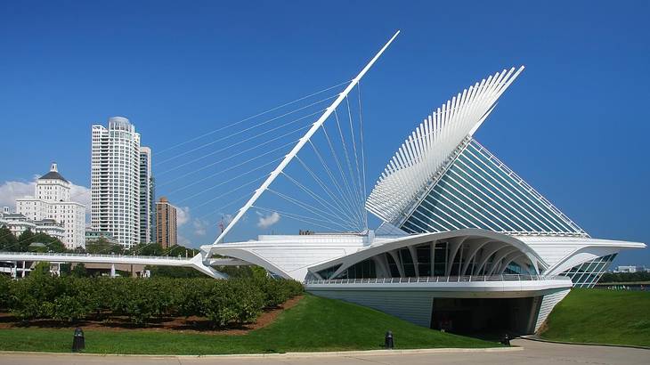 A contemporary white structure with greenery around it and tall buildings next to it