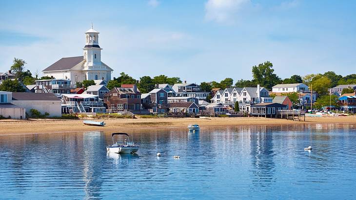 A New England town with a white church next to the water with boats on it