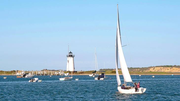 A sailboat on the water with a lighthouse on the shore A sailboat on the water with a lighthouse on the shore