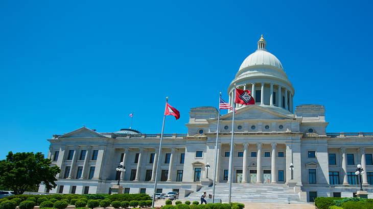 A path leading to a white neoclassical building with 3 flags in front on a clear day A path leading to a white neoclassical building with 3 flags in front on a clear day