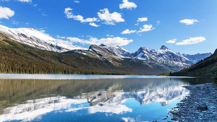 A lake reflecting a tree-covered mountain and the snowy mountains at the back