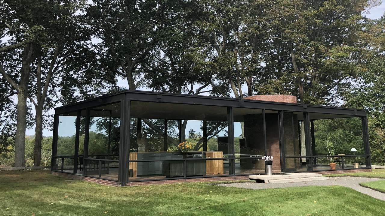 Trees at the back of a house made of steel and glass with a grassy lawn in front