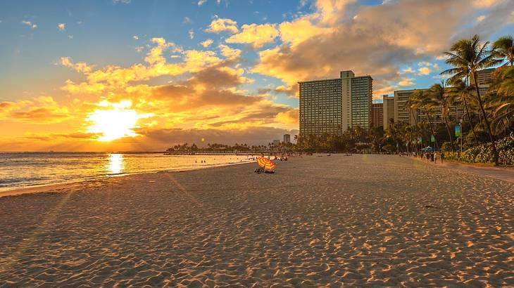 A sandy beach with trees and a building on one side and ocean on the other at sunset