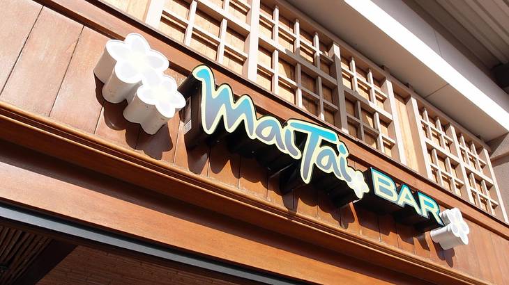 A sign that says "Mai Tai Bar" with flowers on a wooden wall