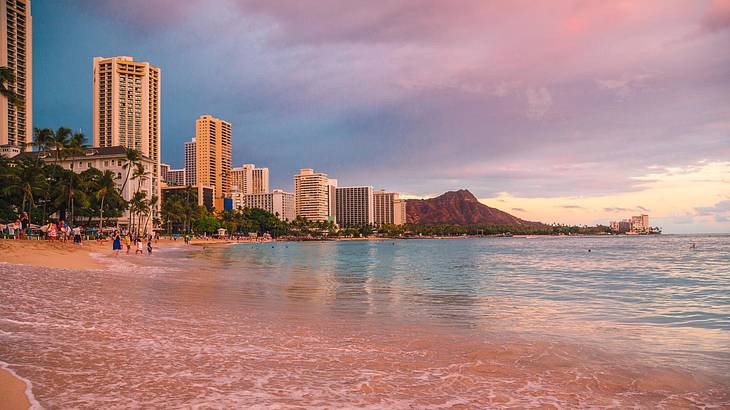 A beach with buildings and a mountain in the distance under a purple sky