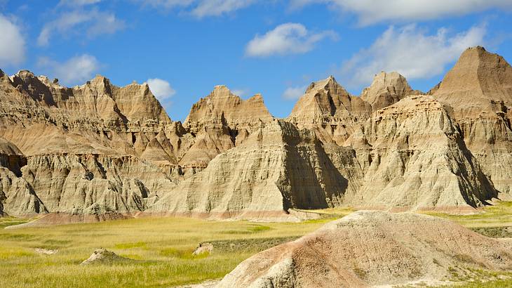 Several striped rock formations with a grassy field below on a sunny day