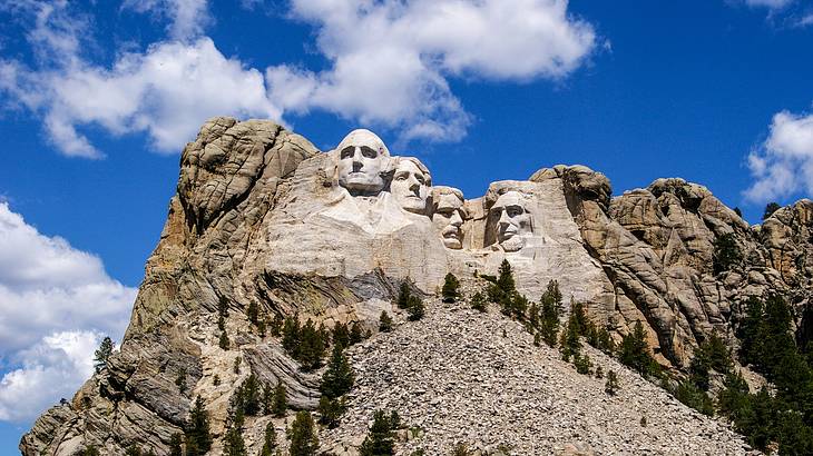 View from below of a rocky mountain with faces of four people carved into its side