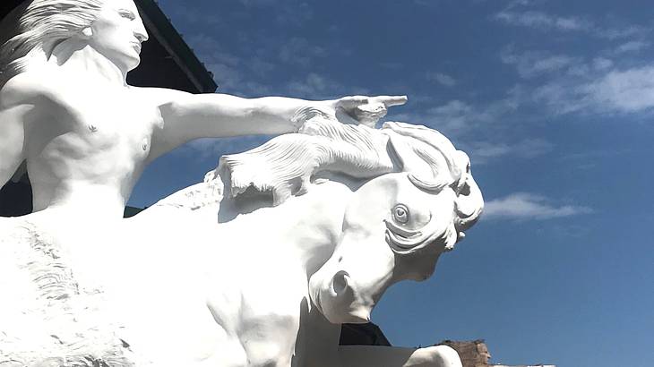 A white statue of a topless man pointing forward and riding on a horse