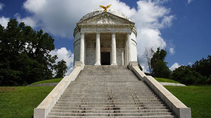 White stairs leading to a marble dome with four columns and a bronze bird sculpture