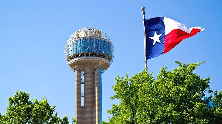 An observation tower with a sphere next to trees and a Texas flag