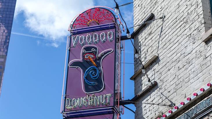 A purple sign on a building that says "Voodoo Doughnut" with a monster-like character