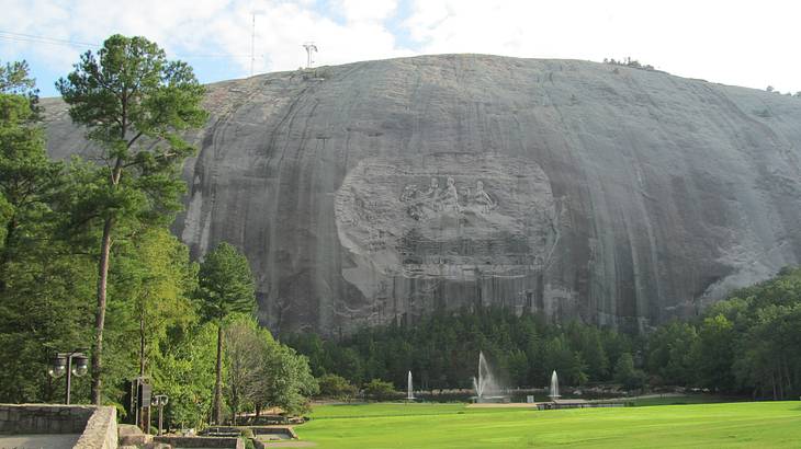 Park with trees at the foot of a rock mountain with people on horseback carved on it