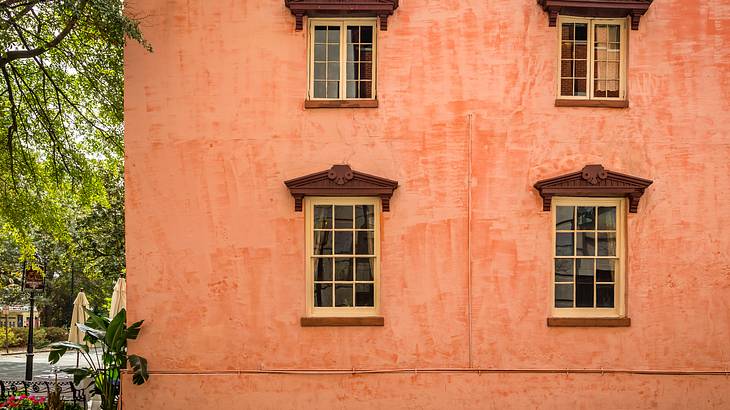Four windows with wooden awnings on a pink house wall with a garden on its side