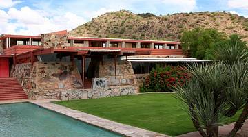 A mountain behind a modern home with stone walls next to grass and a pool