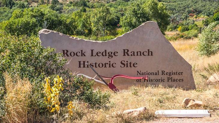 A stone sign that says "Rock Ledge Ranch Historic Site" surrounded by greenery