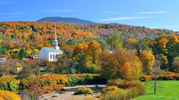 A white church surrounded by orange fall trees and green grass on a clear day A white church surrounded by orange fall trees and green grass on a clear day