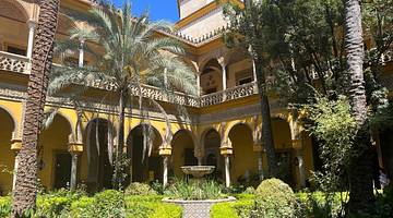 A courtyard with a fountain and palm trees next to a building with yellow arches