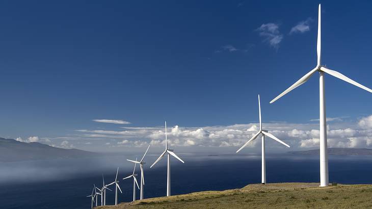 White wind turbines atop a mountain, with the sky and mountains in the background