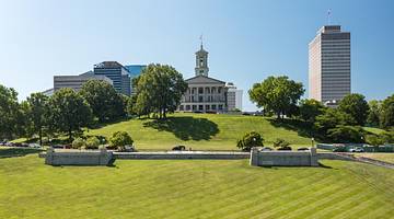 A grassy area with trees and a state capitol building in the distance on a clear day