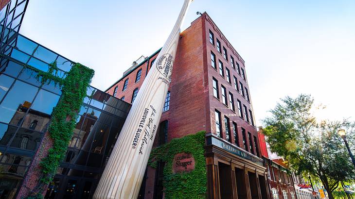 Looking up at a giant baseball bat leaning on the side of a brown building