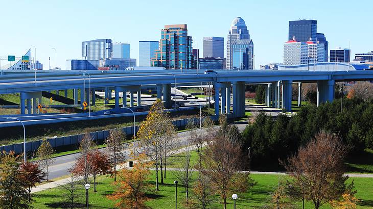 A park with trees in front of a highway with buildings and a clear sky in the back A park with trees in front of a highway with buildings and a clear sky in the back